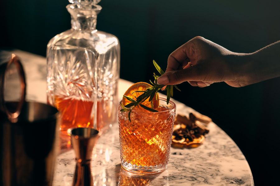 Person putting a sprig into a whisky cocktail